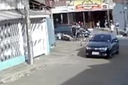 carro parado na rua e dois homens agredindo um terceiro que já está caído no chão