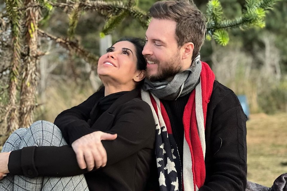 Foto colorida de Maíra Cardi e Thiago Nigro. Ele está de preto e com um cachecol vermelho Ela está de preto e calça de moletom cinza - Metrópoles