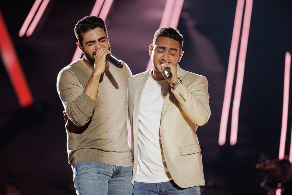 Imagem de Henrique e Juliano. Os irmãos estão com roupa clara, cantando e calça Jeans - Metrópoles