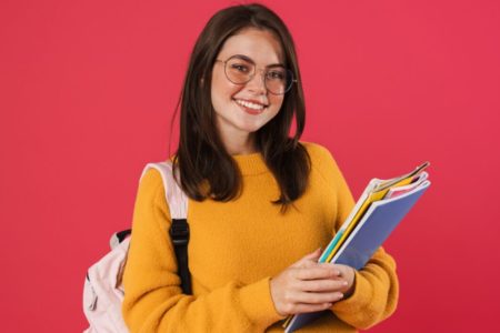 Menina segurando alguns livros de estudo usando óculos e mochila - Metrópoles