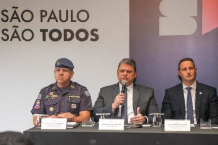 Foto colorida do governador Tarcísio de Freitas (de terno cinza), entre o coronel Cássio (à esquerda, de farda), e o secretário Guilherme Derrite (à direita, de terno preto)