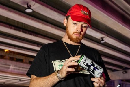 Angus Cloud em foto colorida. Ele está de boné vermelho, camisa preta e segura uma lata de bebida - Metrópoles