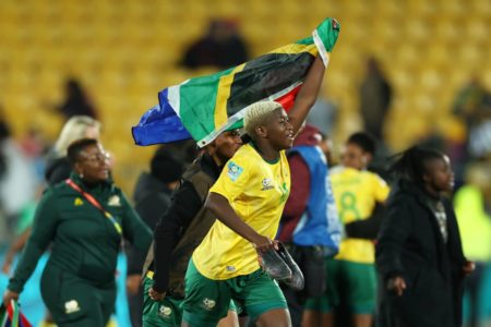 Mulher negra, vestida de uniforme amarelo, corre de braço erguido com bandeira na mão - Metrópoles