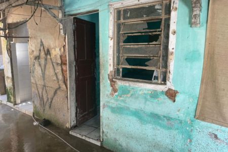 foto colorida - fachada de casa com pintura verde desgastada; é possível ver janelas quebradas e porta aberta