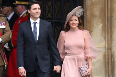 imagem colorida mostra primeiro-ministro do canadá justin trudeau usando terno azul escuro, ele é branco e tem cabelos pretos e olhos verdes. ao lado, a esposa sophie trudeau com vestido rosa claro e chapéu, ela é branca e tem os cabelos castanhos e lisos