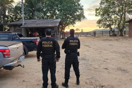 Policiais federais ao lado de veículos em área aberta