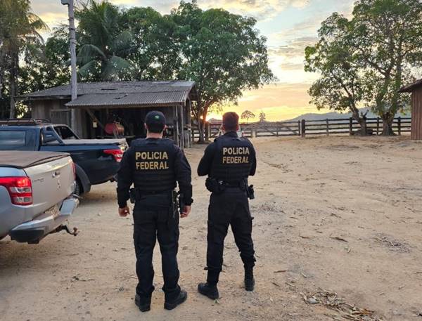 Policiais federais ao lado de veículos em área aberta