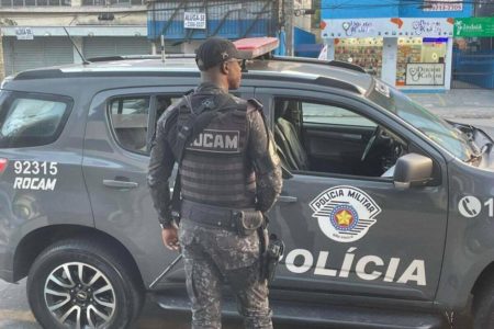 Foto colorida mostra policial militar da Rocam parado em frente a viatura