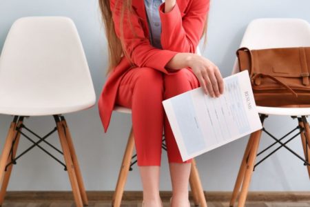 Mulher segurando curriculum na mão para vaga de emprego com terno vermelho sentada na cadeira - Metrópoles