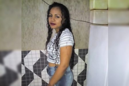 Mulher negra de cabelos negros cacheados veste camisa listrada e calça jeans