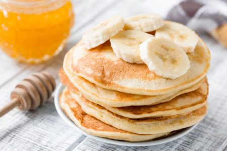 Panqueca de banana com algumas bananas picadas em cima com um mel ao lado em um pote de vidro - Metrópoles