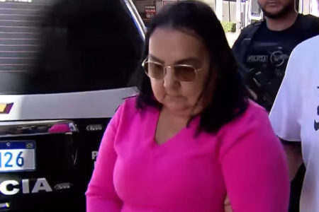 Mulher com blusa rosa e óculos escuros olha para baixo com semblante triste - Metrópoles