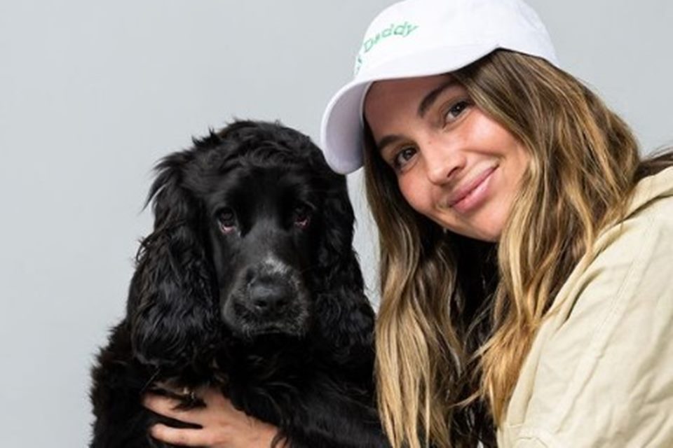 Na imagem colorida, uma mulher branca de cabelo loiro abraça um cachorro preto - Metrópoles