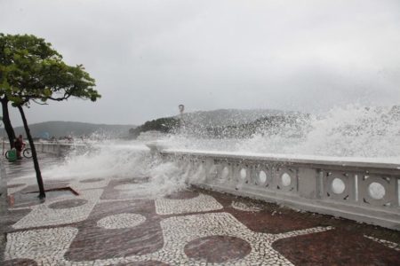 Foto colorida mostra mar agitado com ressaca em Santos, a água do mar atravessa mureta do calçadão de praia em Santos