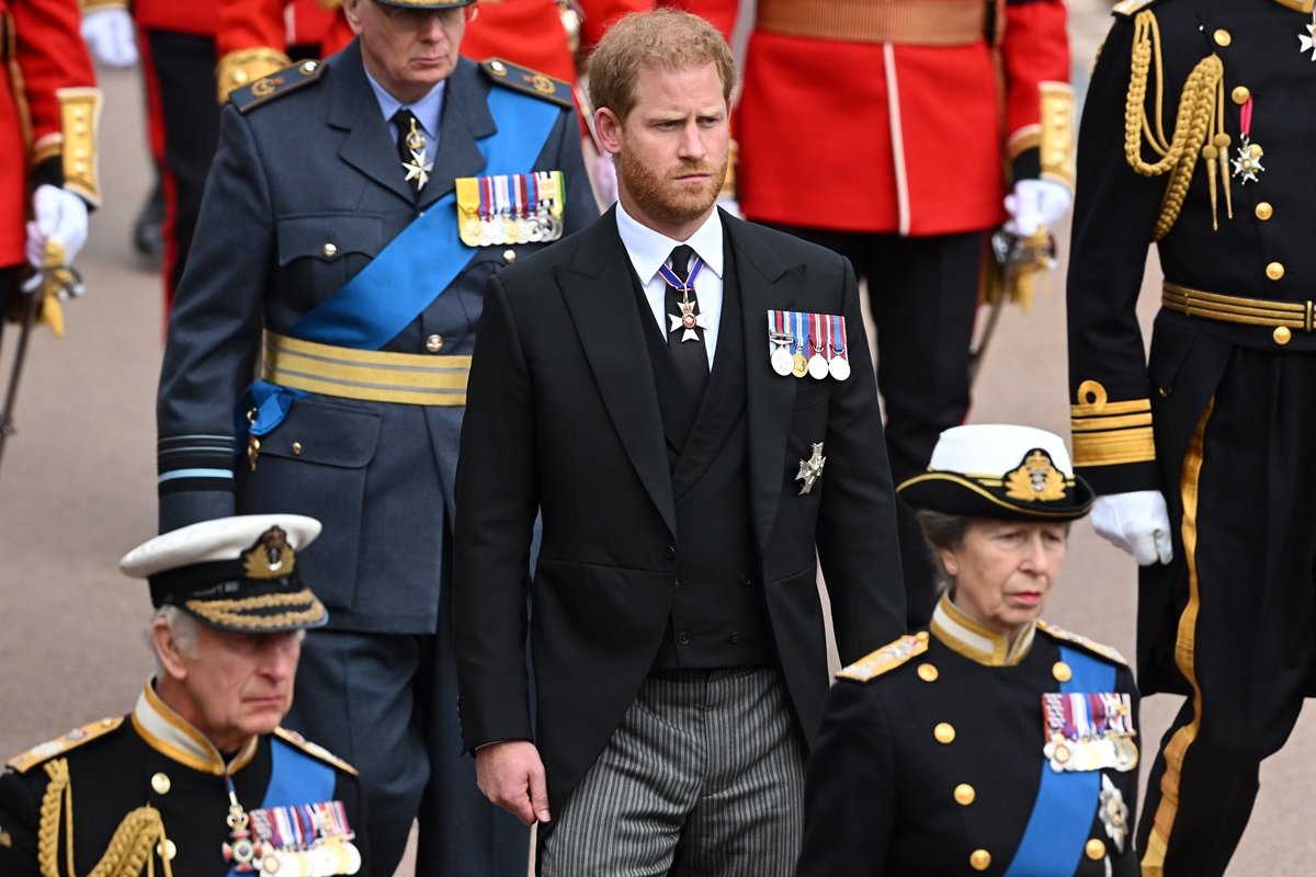 Foto colorida. Imagem foca em um homem branco, ruivo, com terno preto e medalhas millitares. Ao seu redor estão outros membros da realeza vestidos de trajes militares - Metrópoles