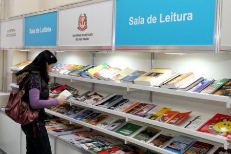 imagem colorida mostra mulher com livro na mão em frente à prateleira da sala de leitura do governo de são paulo - metrópoles