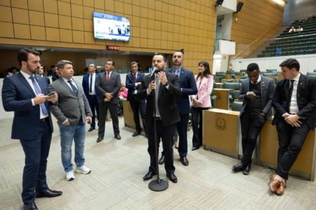 Foto colorida - deputados da Alesp de terno e gravata em sessão estraordinária; um deles fala ao microfone