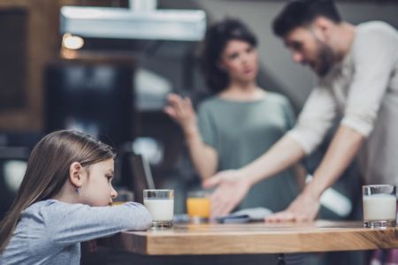 Menina se sentindo triste enquanto seus pais estão discutindo em segundo plano. - Metrópoles