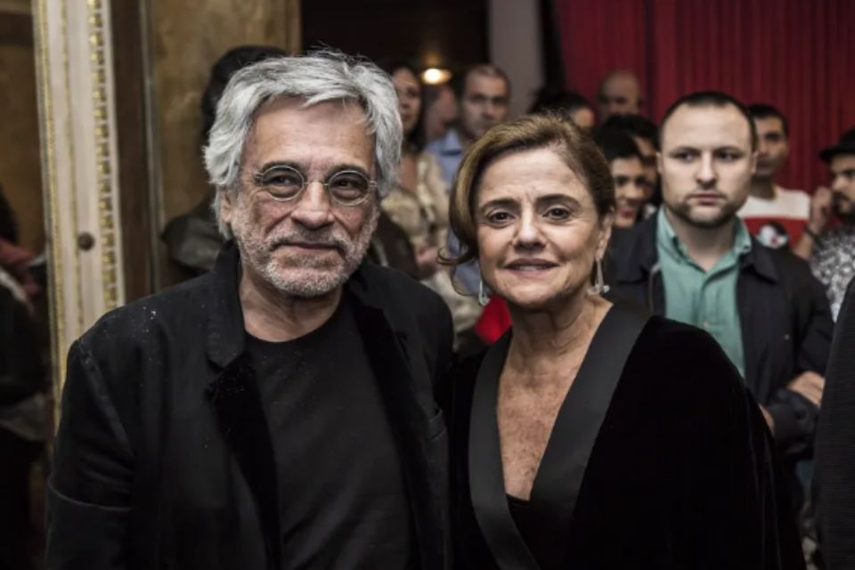 Aderbal Freire Filho e Marieta Severo. Ele está de blazer e blusa preta, com óculos de grau. Ela está sorrindo, de look preto - Metrópoles