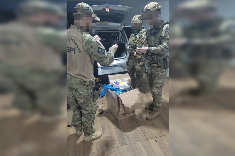 Policiais rodoviários federais com uniforme camuflado abrindo caixa com diversos itens retirada de um carro prata