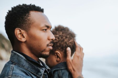 Um homem negro segurando um bebe negro na praia olhando pro nada, dia dos pais - Metrópoles