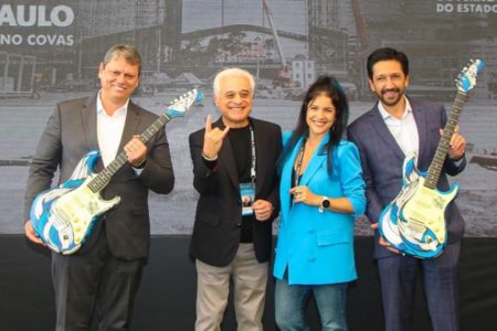 Foto colorida - Governador Tarcísio (esq.) e Ricardo Nunes (dir.) entre os organizadores do festival The Town; Tarcísio e Nunes seguram guitarras azuis