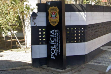 Imagem colorida mostra placa que sinaliza entrada da Delegacia Seccional de Guaratinguetá; paredes são pintadas em listrado (preto e branco) - Metrópoles