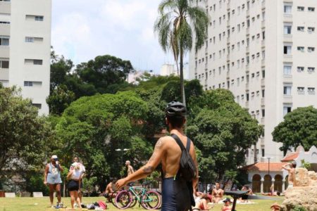 foto colorida - frequentadores no Parque Augusta aproveitam o sol em gramado; há um jovem caminhando sem camisa e pessoas deitadas na grama sob o sol