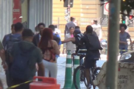 Em foto colorida criminoso em bicicleta pega celular de vítima em calçada no centro de São Paulo - Metrópoles