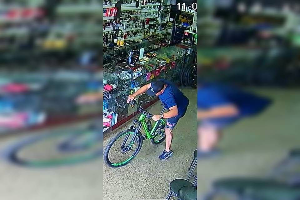 Homem de roupa azul e boné em cima de uma bicicleta verde