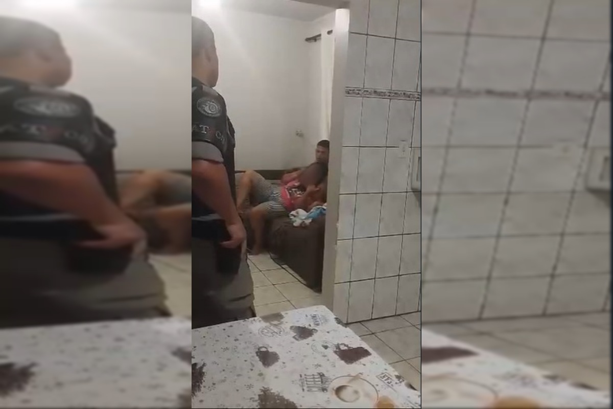 Policial militar segura arma na cintura. Ele olha para homem que está com faca no pescoço da própria mãe