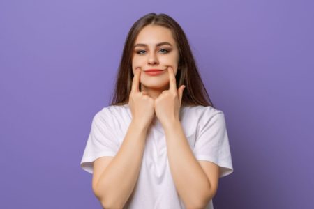 Mulher fazendo sorriso com as mãos na boca com blusa branca - Metrópoles