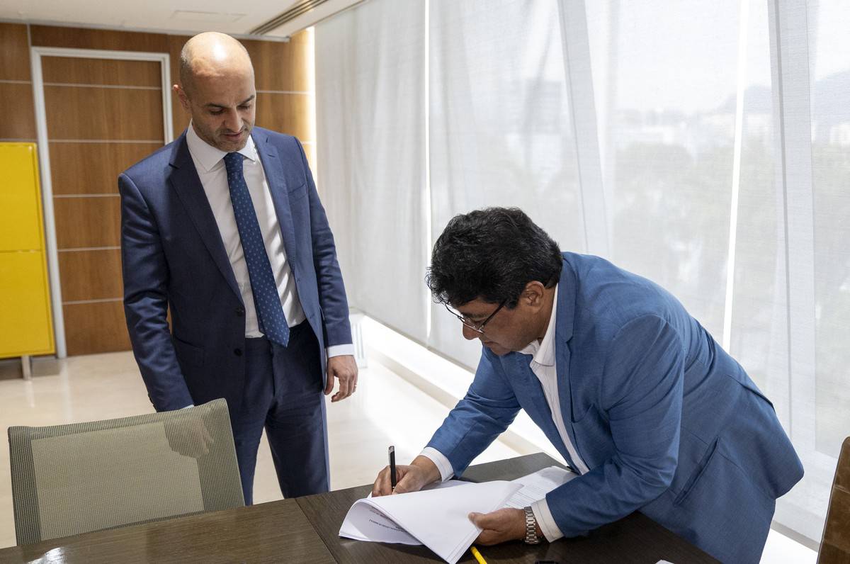 Fotografia colorida mostrando dois homens de terno assinando contrato-Metrópoles