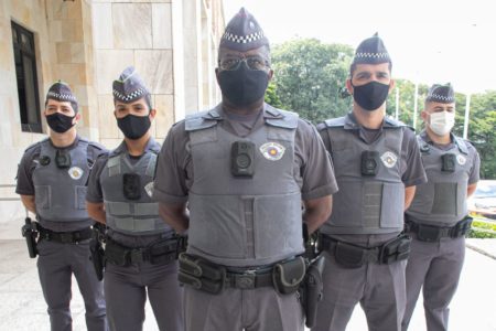 Imagem colorida de PMs usando câmeras corporais. Os policiais estão enfileirados - Metrópoles
