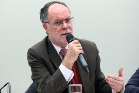 Imagem colorida mostra Barjas Negri, homem branco, calvo, grisalho, de barbas brancas, de terno marrom e gravata vermelha, falando ao microfone em uma mesa - Metrópoles