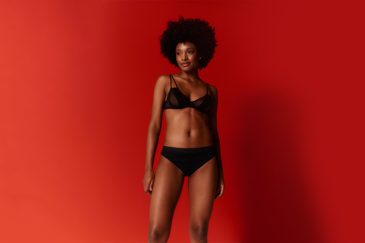 Em fundo vermelho, mulher usa conjunto preto de lingeries com calcinha e sutiã - Metrópoles