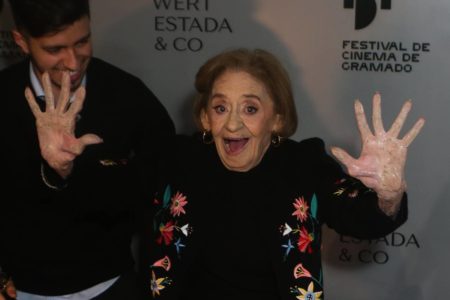 Foto colorida de Laura Cardoso com as mãos pra cima no Festival de Gramado - Metrópoles