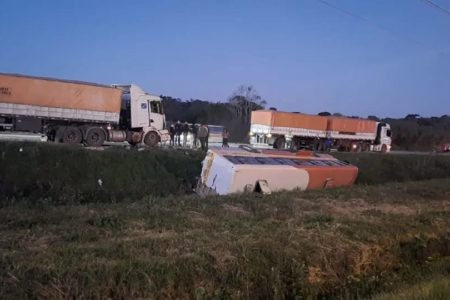 Imagem colorida de ônibus escolar capotado em pista - Metrópoles