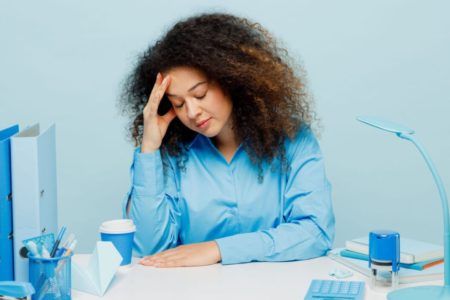 mulher vestindo azul com varias coisas em cima da mesa de escritório de cor azul também - Metrópoles