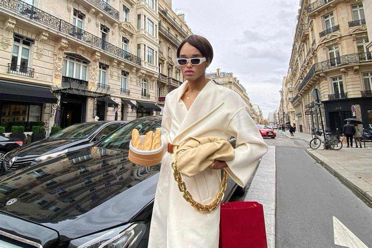 Homem parado na rua segurando uma cesta de pães com uma das mãos e uma bolsa com a outra - Metrópoles