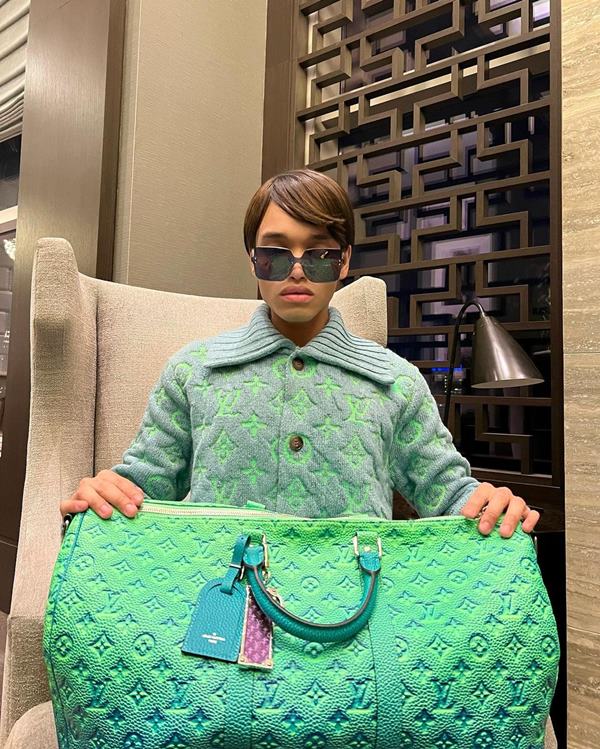 João VS, influencer acusado de golpes Garoto sentado em cadeira com uma bolsa grande nas mãos - Metrópoles
