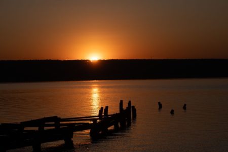 Foto Lago Paranoá com o sol nascendo ao fundo. Pessoas nadam na água