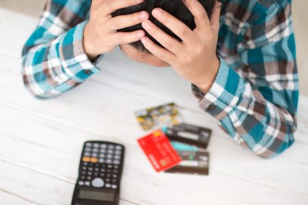 Homem com camisa quadriculada põe as mãos na cabeça, debruçado sobre uma mesa, de cabeça baixando, olhando para as contas a pagar, os cartões de crédito e uma calculadora - Metrópoles