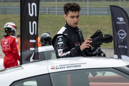 Cena do filme Gran Turismo. Um homem de macacão preto está próximo de um carro branco - Metrópoles