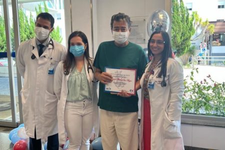 Foto de homem segurando certificado de alta ao lado de três médicos em hospital - Metrópoles