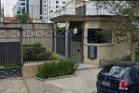 Portão cinza escuro de condomínio residencial, com guarita pintada de amarelo - Metrópoles