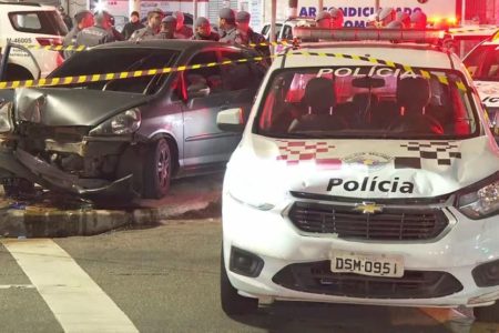 Dois carros estacionados em avenida; à frente, uma viatura branca da Polícia Militar de São Paulo; ao fundo, um carro cinza escuro com a parte frontal destruída - Metrópoles