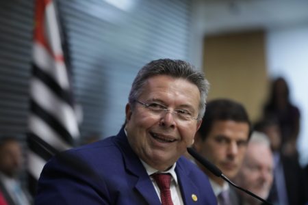 Imagem colorida mostra foto Carlão Pignatari, homem branco, grisalho, de óculos, do busto para cima, de terno azul e gravata, sorrindo para a foto - Metrópoles