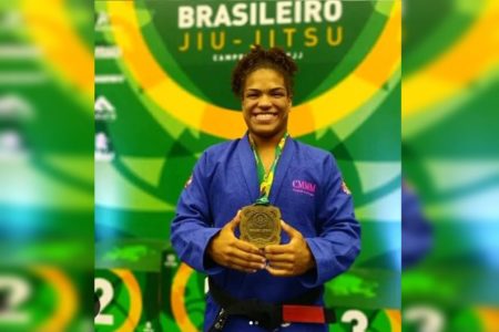 mulher negra com quimono azil segurando um troféu de campeonato de jiu-jitsu