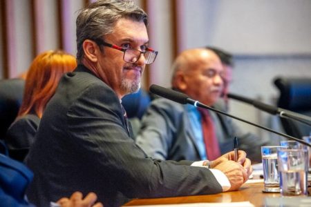 Foto colorida de pessoas de terno e gravata e demais roupas sociais sentados em frente a uma bancada- Metrópoles